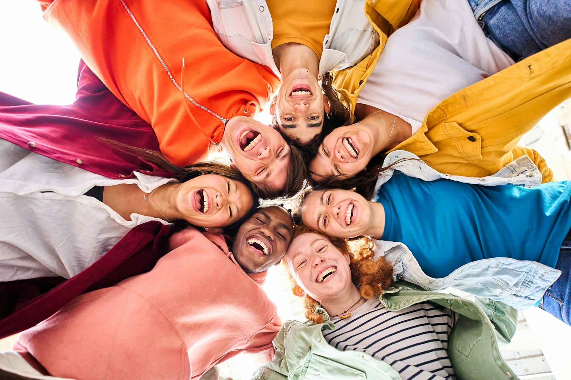 Large multiracial group of smiling young people standing hugging looking at camera. Low angle view.