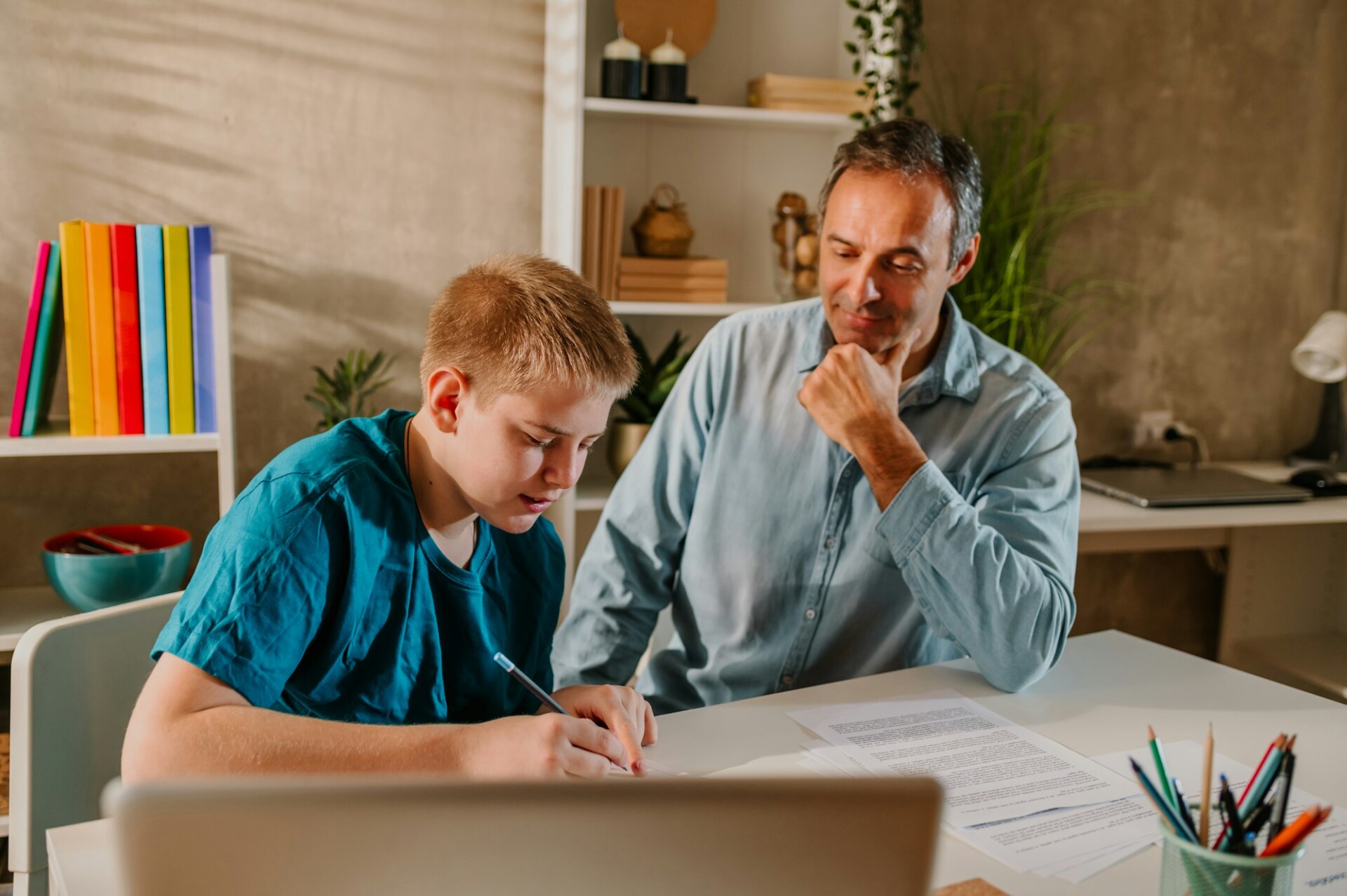 Supportive father watching his son with joy while he is writing his homework.